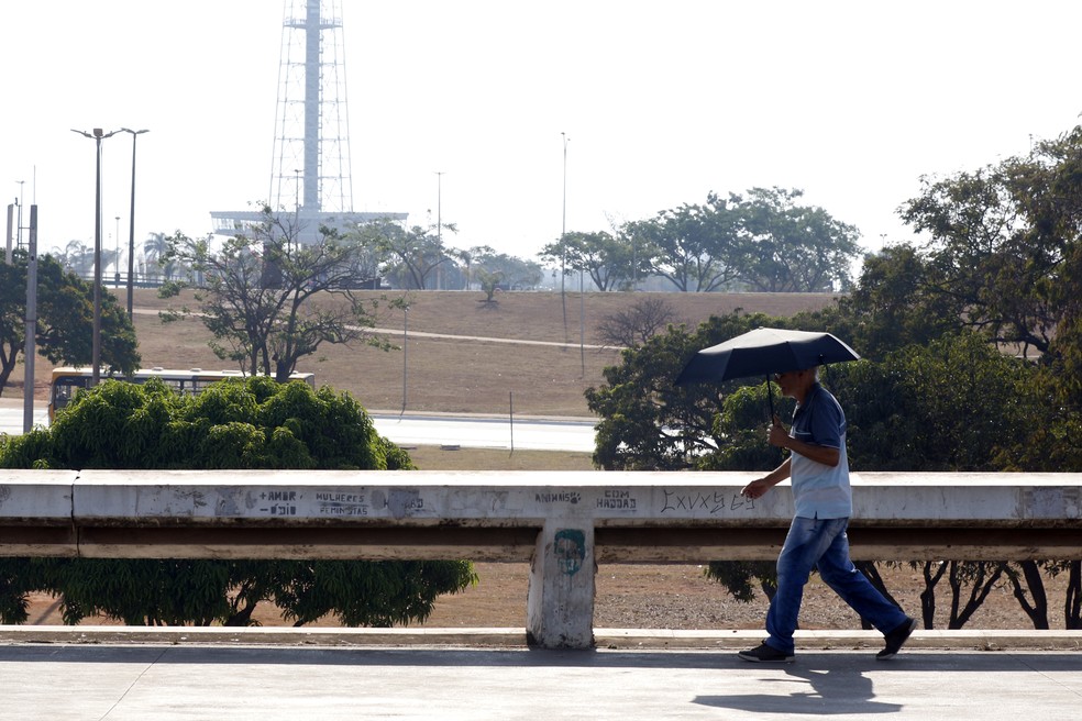 03.09.2024 – Em meio à seca e ao calor intenso， pedestre usa guarda-sol ao atravessar o Setor de Diversões Sul， em Brasília. — Foto: Bruno Peres/Agência Brasil
