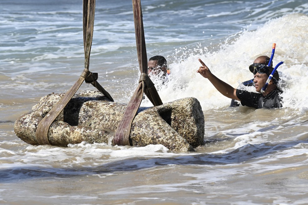 Mergulhadores observam enquanto um guindaste puxa uma estátua das águas da baía de Abu Qir， em Alexandria， no dia 21 de agosto de 2025， como parte de um evento organizado pelo Ministério do Turismo e das Antiguidades para recuperar antiguidades submersas — Foto: Khaled DESOUKI / AFP
